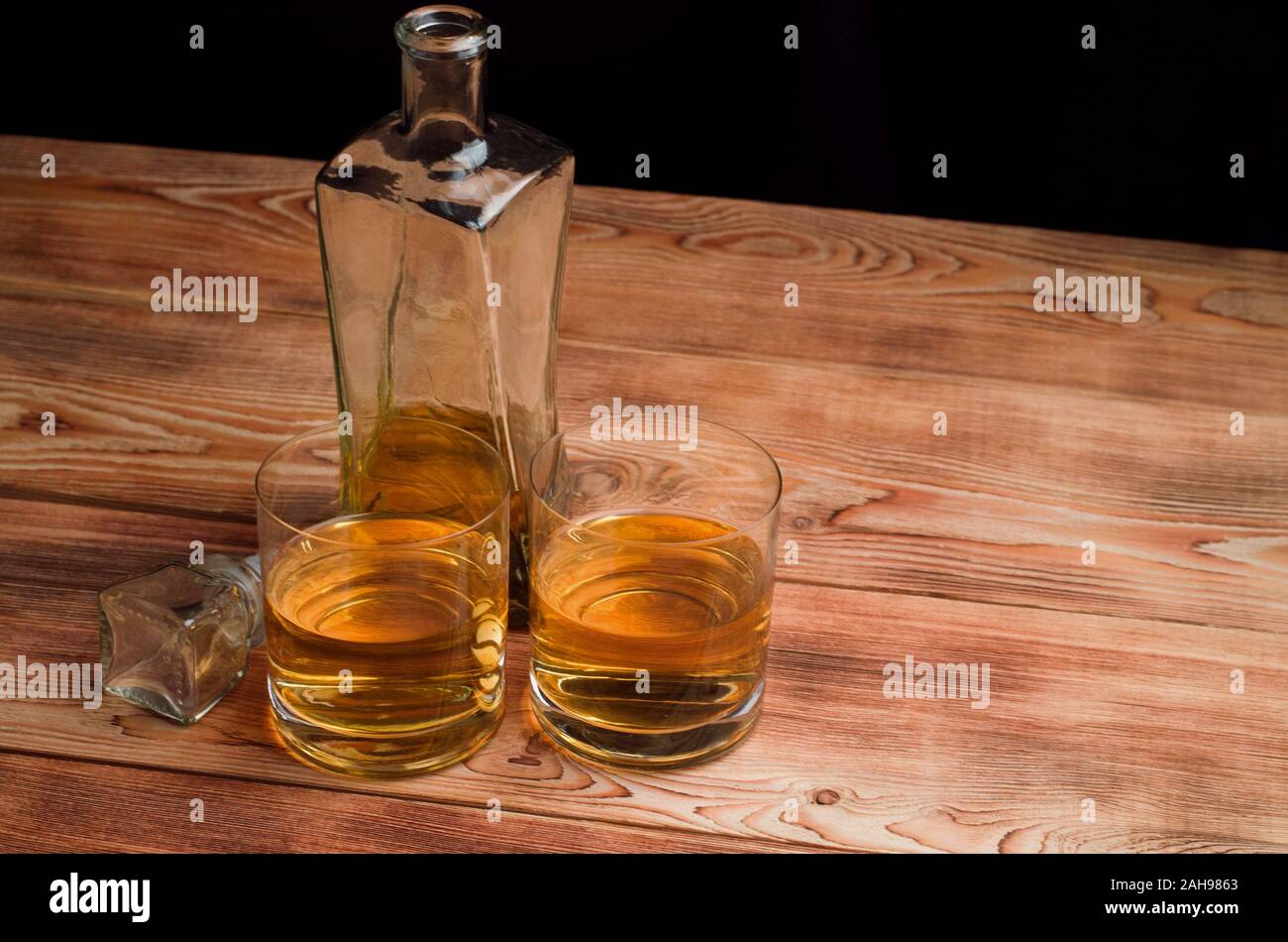 Two glasses of whiskey stand next to the decanter on a wooden table. Glasses with whiskey without ice. Stock Photo