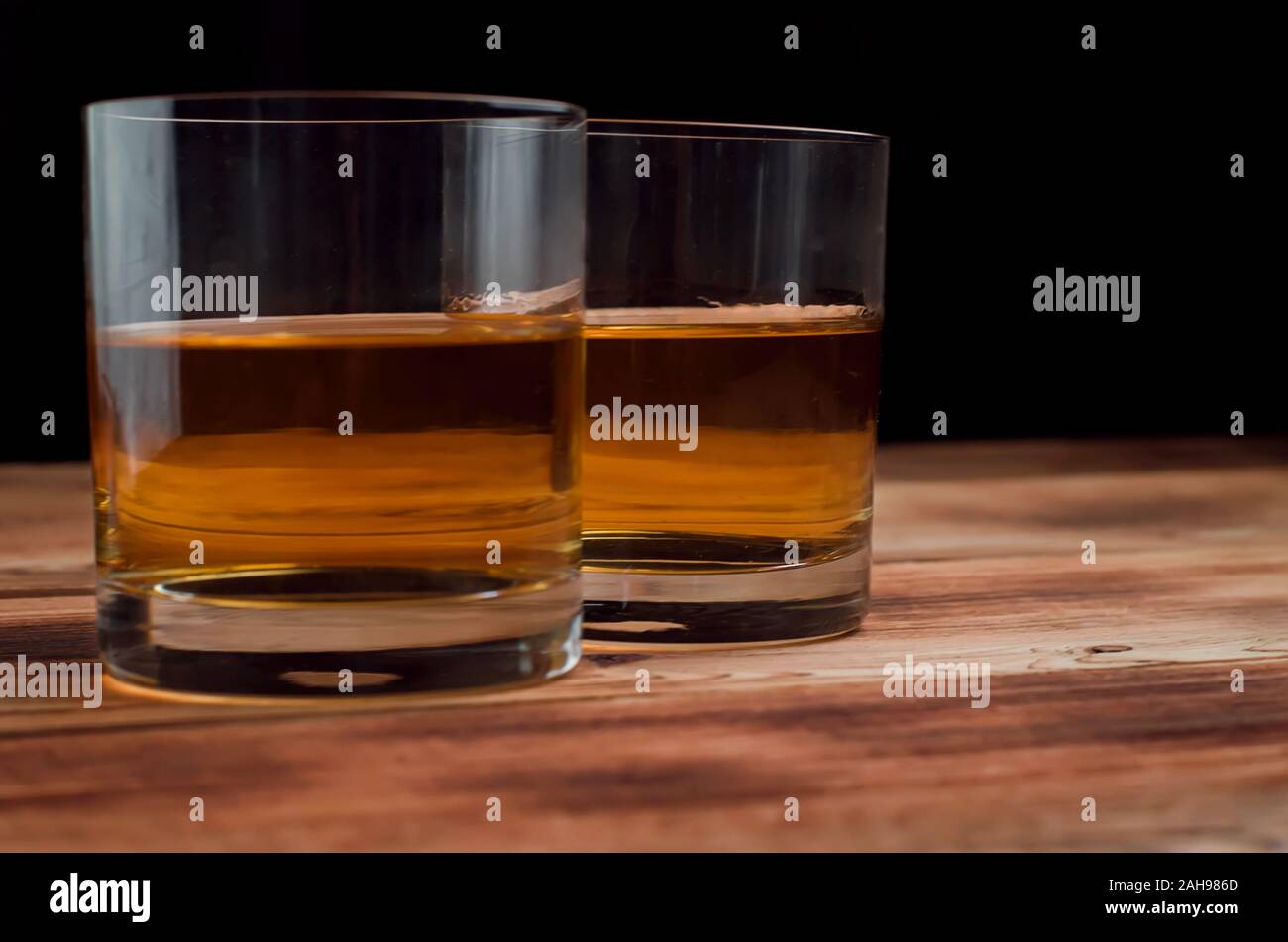 Two glasses with whiskey stand on a wooden table. Glasses with whiskey without ice. Stock Photo