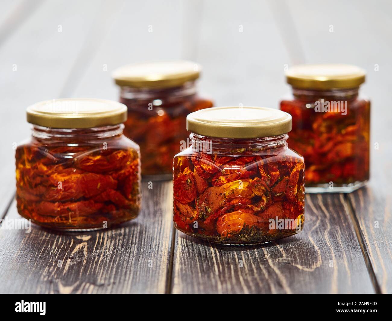 Home-made canned red dried cherry tomatoes are packed in small glass jars. Stock Photo