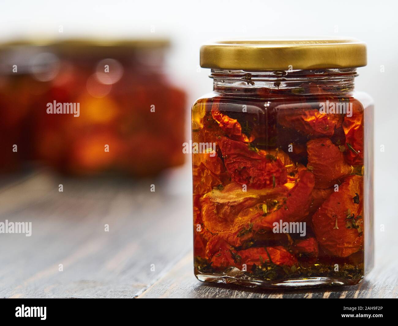 Home-made canned red dried cherry tomatoes are packed in small glass jars. Stock Photo