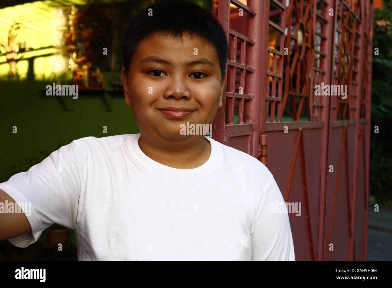 Portrait of young Asian boy smiling at the camera while standing in front of a gate Stock Photo
