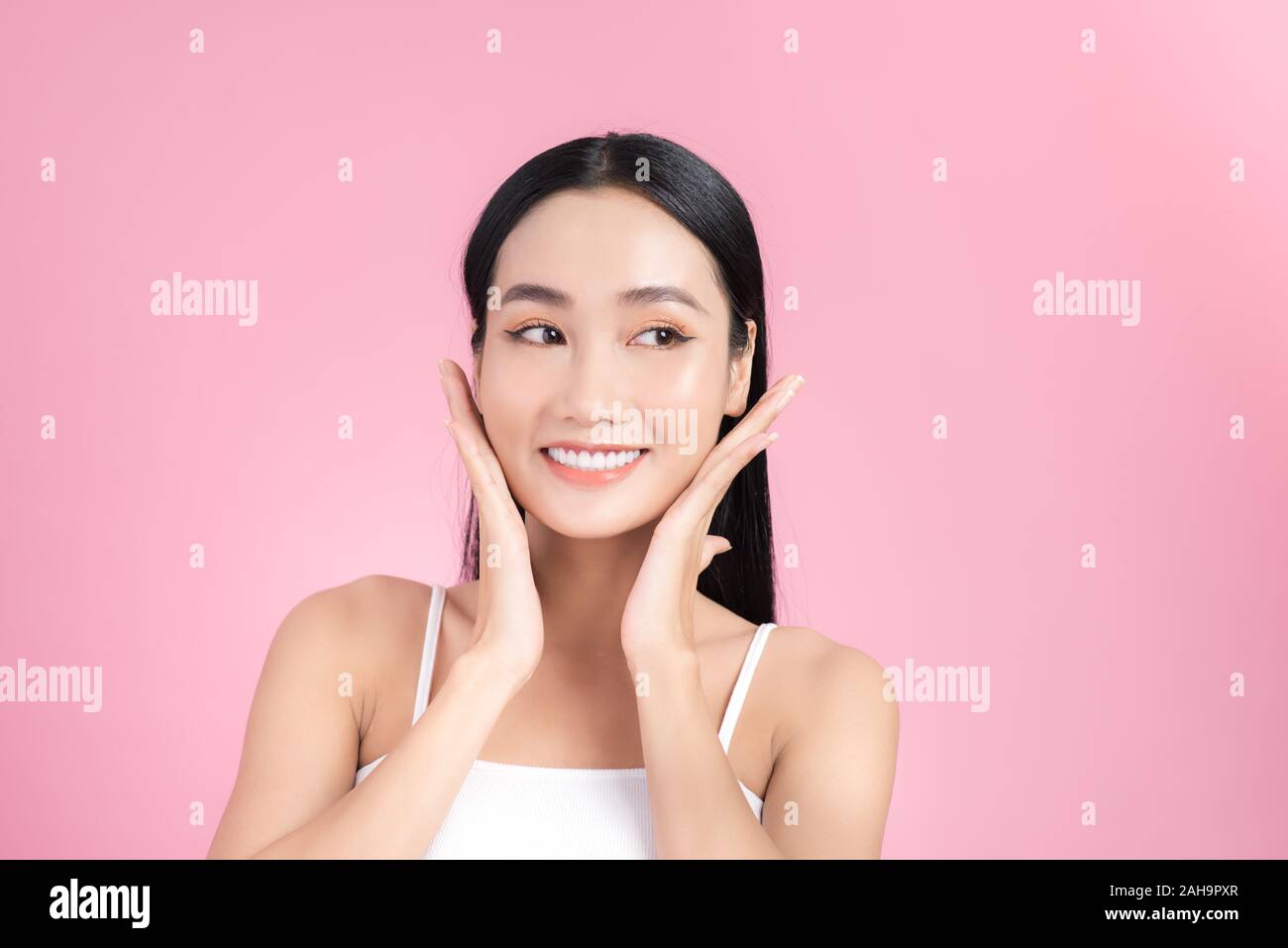 Beautiful young Asian girl touching her perfect skin on pink background ...