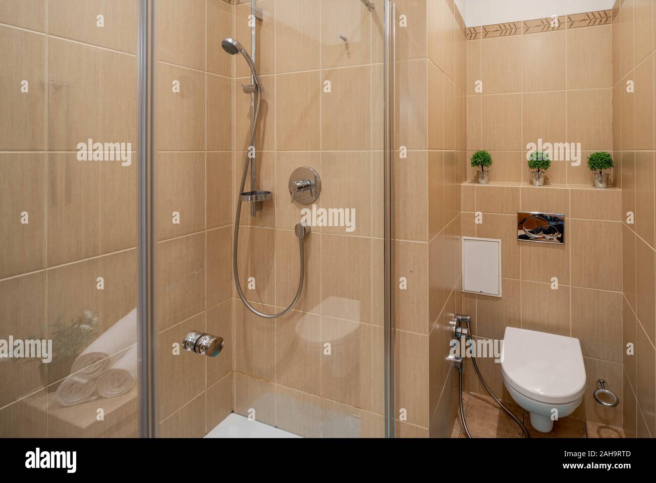 View of toilet and shower in modern interior of bathroom. Light brown tile. Stock Photo