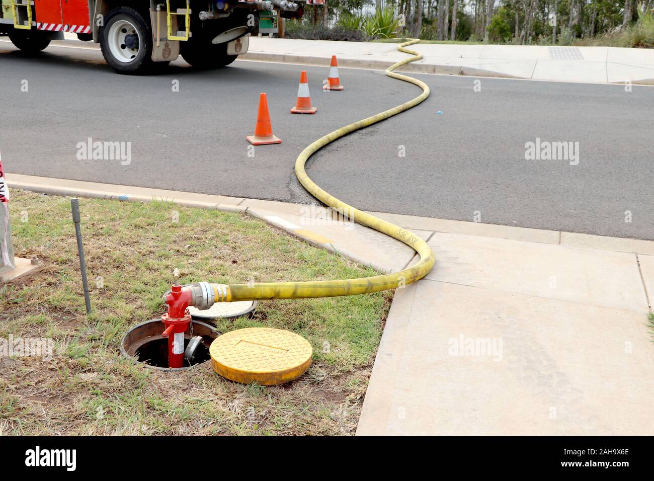 Yellow fire hose attached to red inground water tap and extending across the road Stock Photo