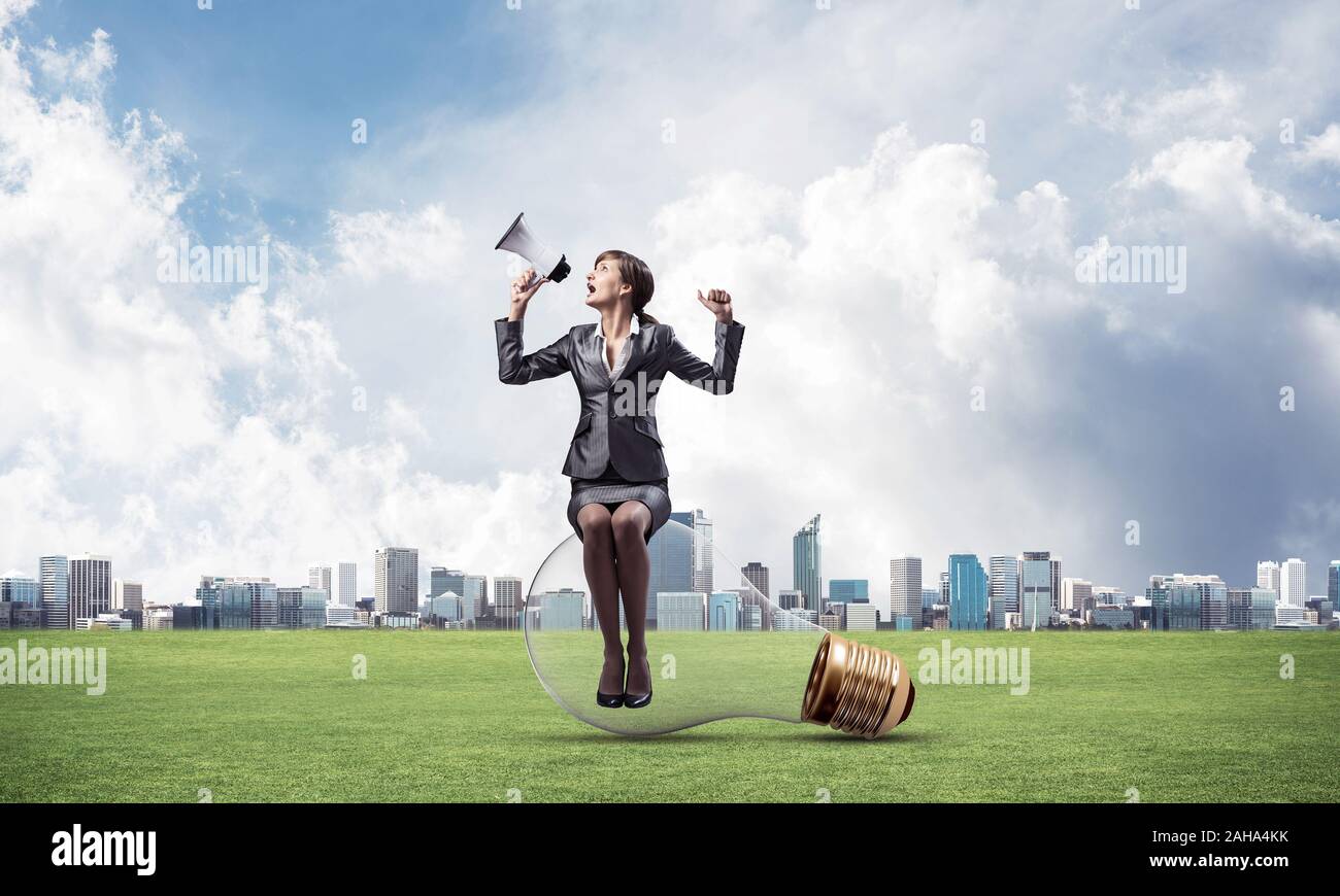 Young woman with megaphone sitting on big light bulb. Female