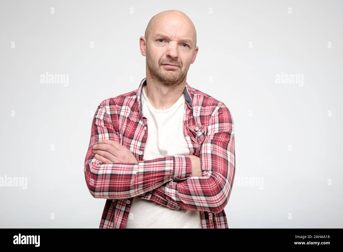 Pensive, frowning bald man is standing with his arms crossed and looking at the camera. Stock Photo