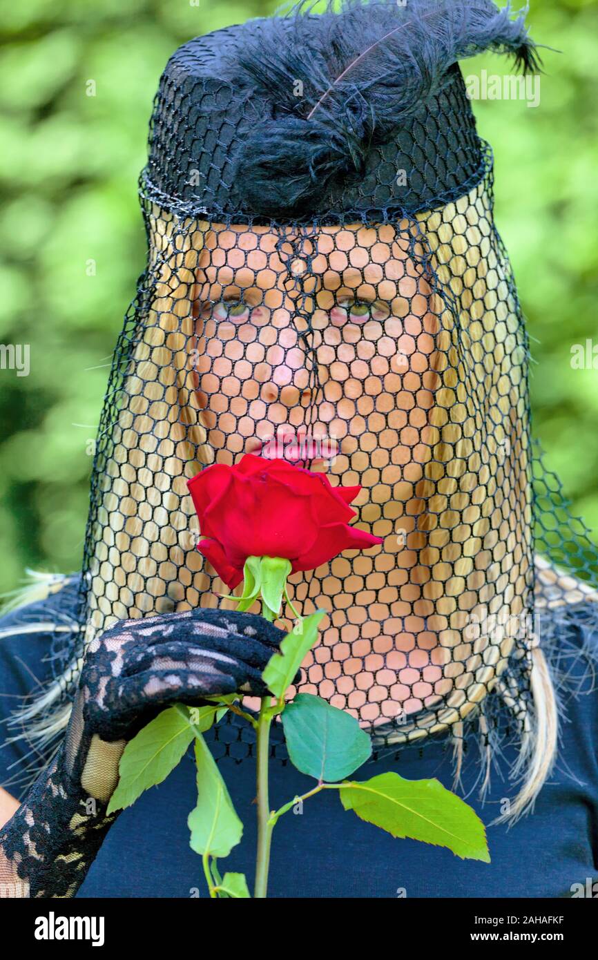 Eine junge trauernde Witwe mit Schleier und roter Rose. Todesfall und Erbschaft, MR: YES Stock Photo