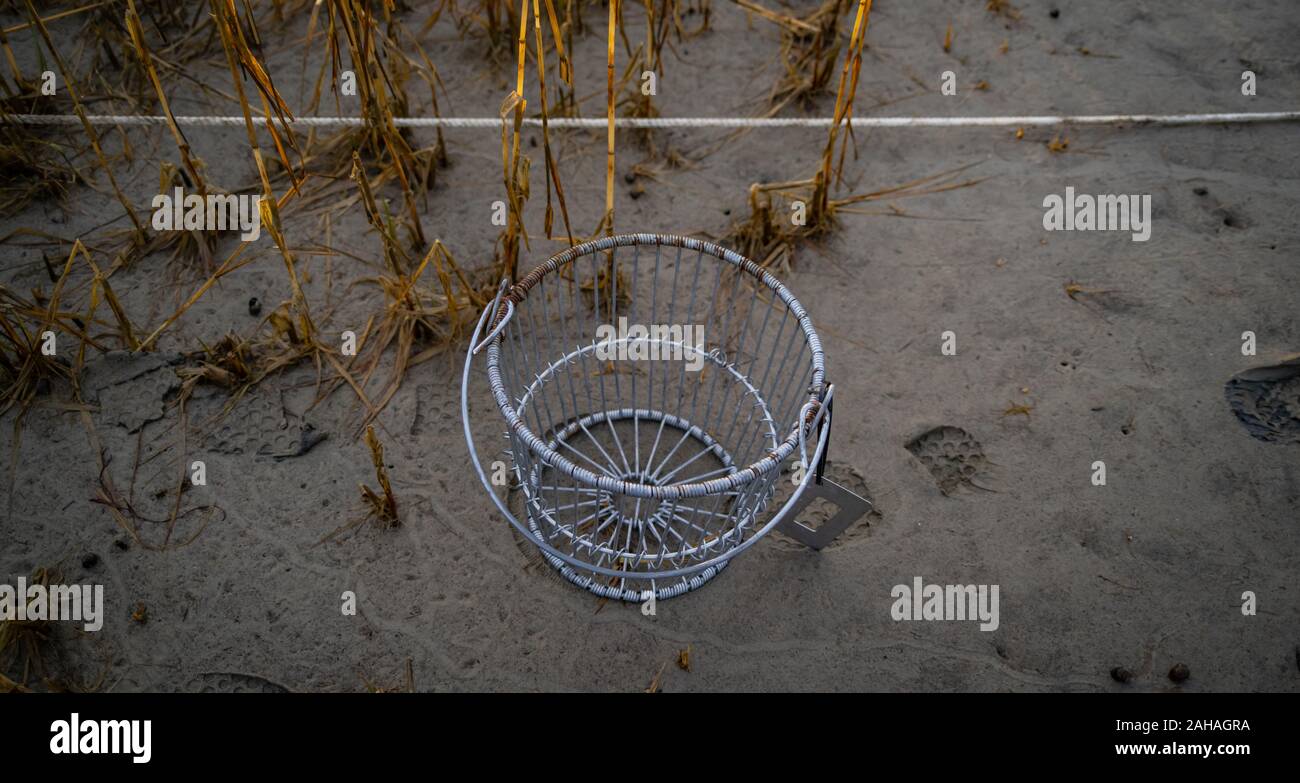 A wire basket with a measuring tool and boot tracks in the sand. Stock Photo