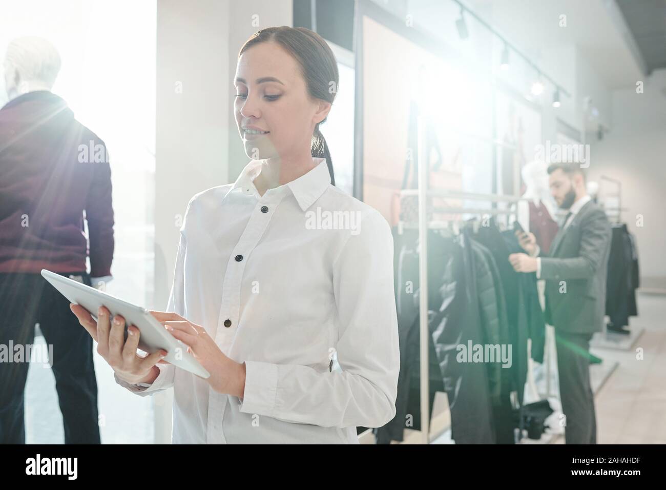 Young elegant shop assistant scrolling in touchpad on background of ...