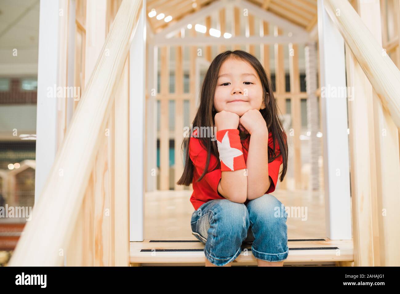 Restful little girl in blue jeans and red t-shirt sitting on wooden stairs Stock Photo