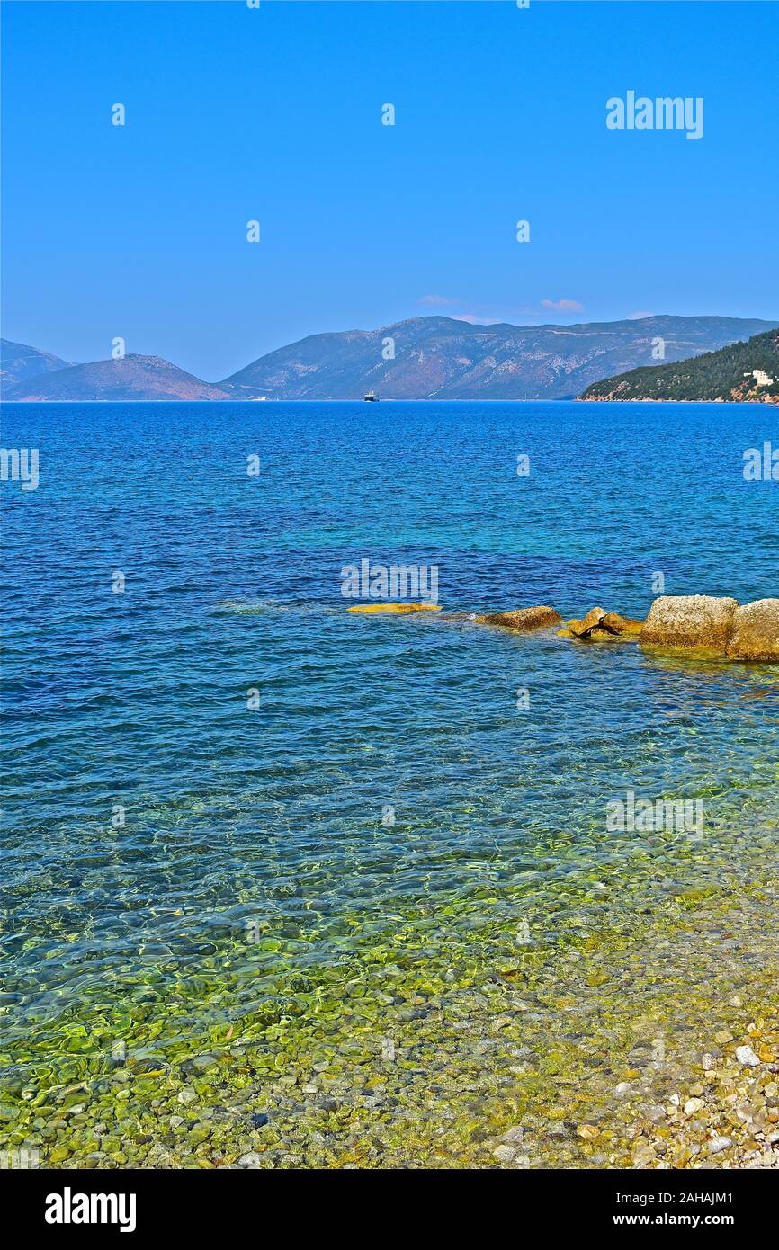 A distant view of Ionian P Lines ferry arriving in the bay before docking in Sami. A wonderful backdrop of mountains. Seen from the pebbly beach. Stock Photo