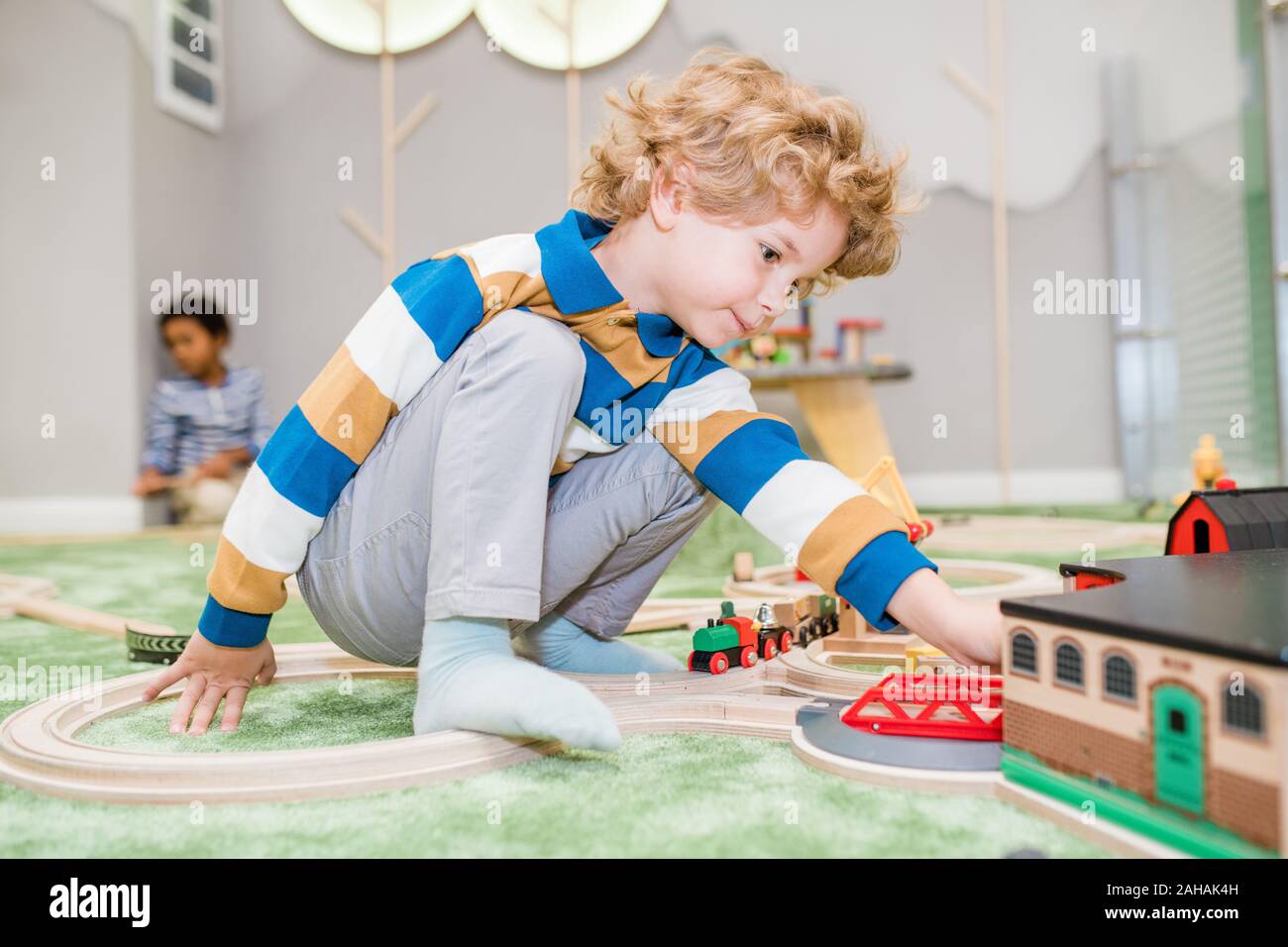Adorable blond little boy in casualwear playing on the floor in kindergarten Stock Photo