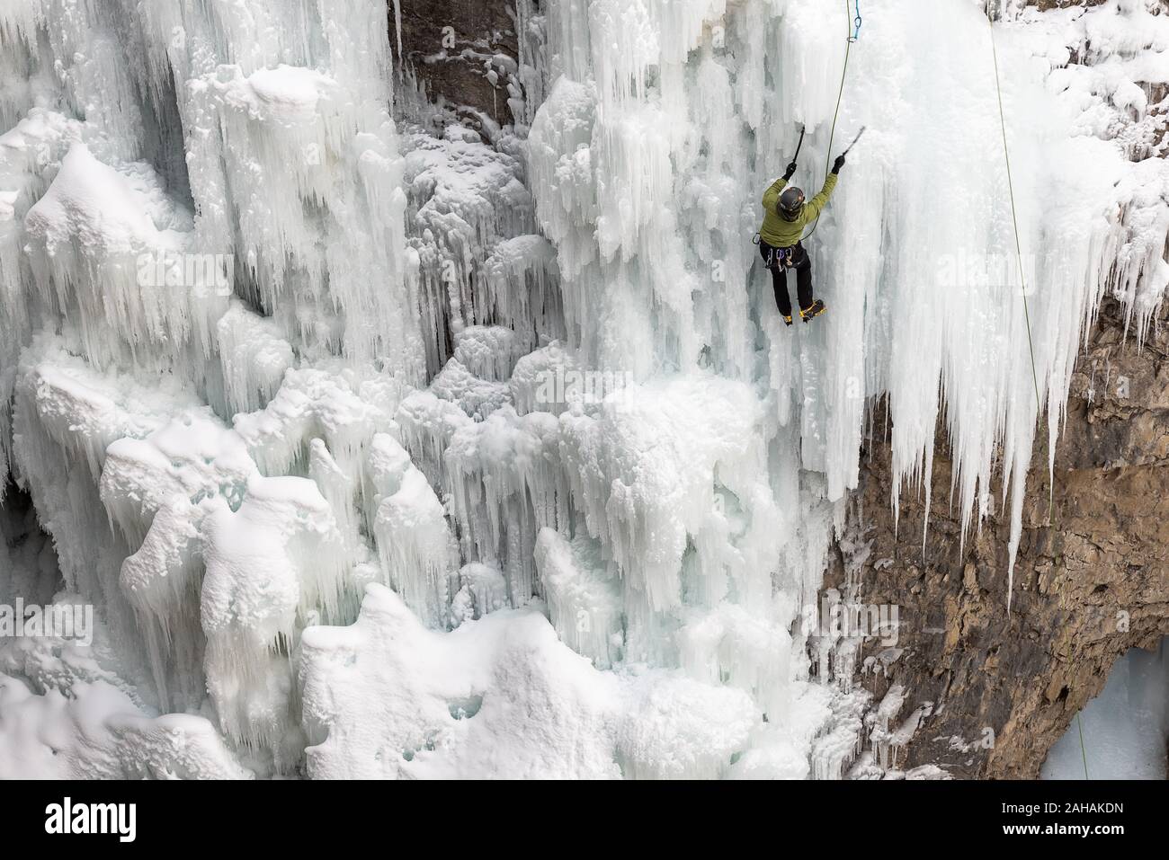 A solo male ice climber uses climbing equipment to work his way up