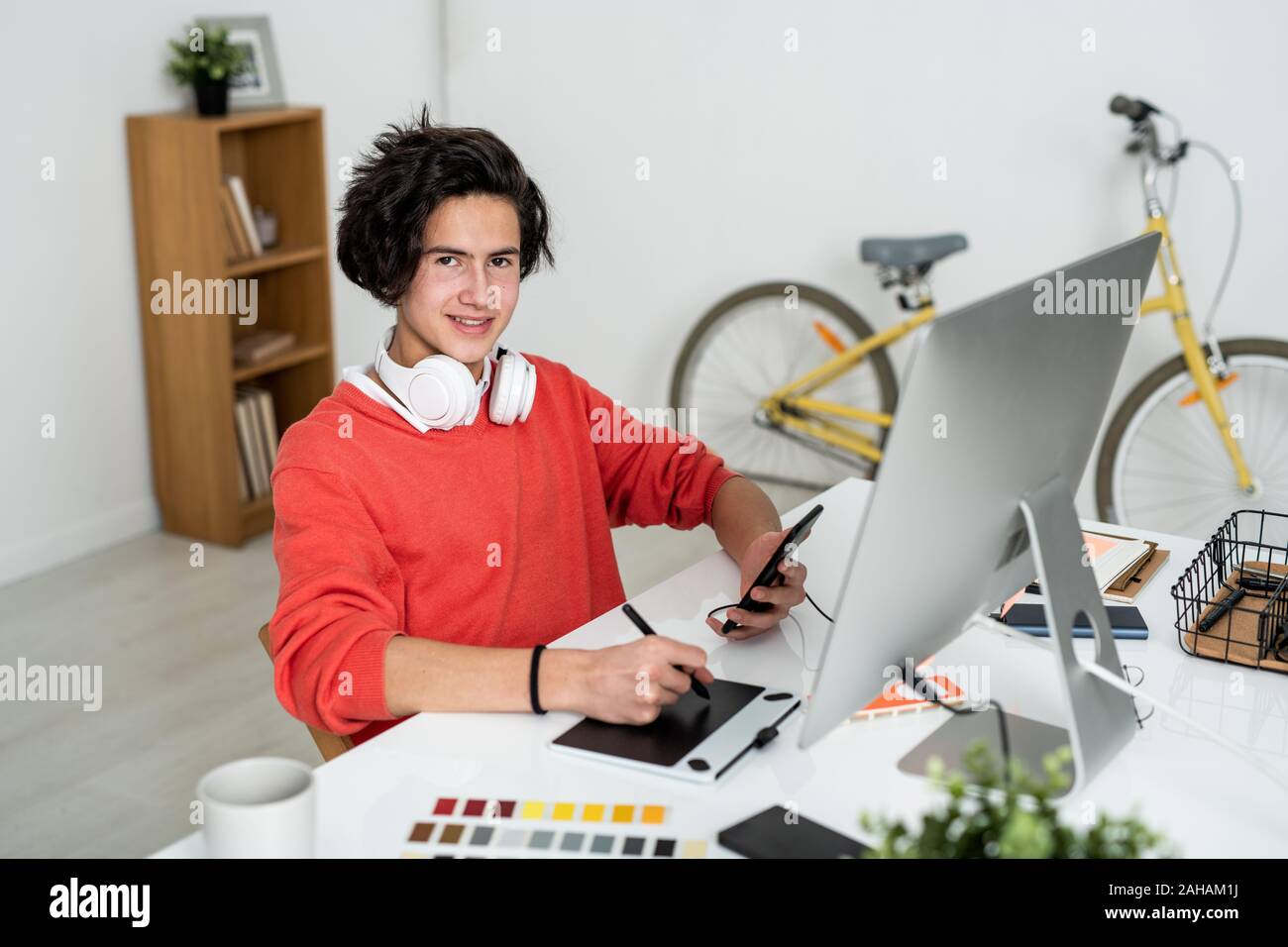 Happy guy with stylus and smartphone looking at you while using graphics tablet Stock Photo