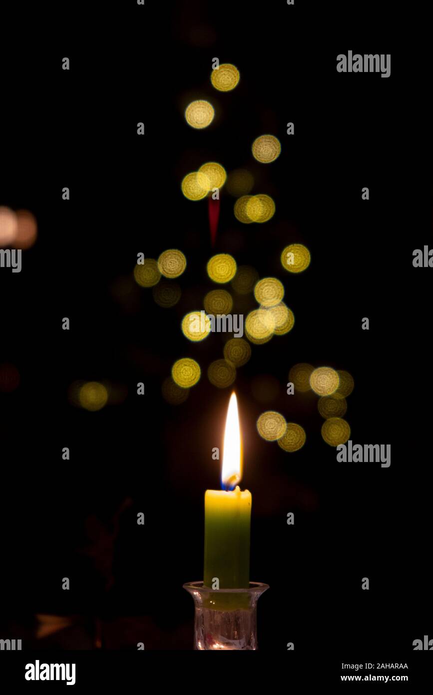 A single candle glows in front of an out of focus Christmas tree Stock