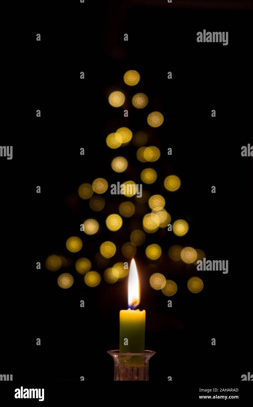 A single candle glows in front of an out of focus Christmas tree Stock