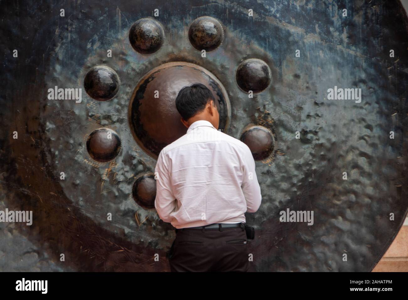 At Kanchanaburi, Thailand- On august 2019 - man meditating in front of a  gong in the ancient temple at Kanchanaburi called Wat Tam Sua, Thailand Stock Photo