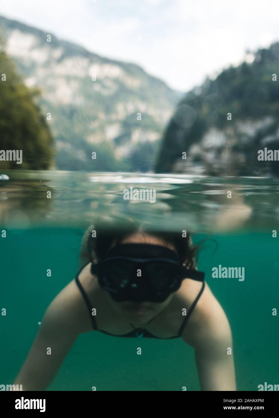 Half half picture of girl swimming in a lake with a mask, in the background are mountains Stock Photo