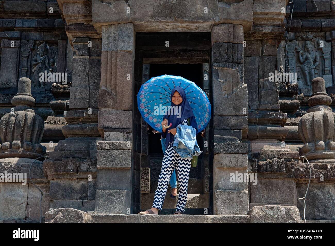 Smiling young indonesian girl wearing blue jilbab with umbrella in Prambanan temple in Java Stock Photo