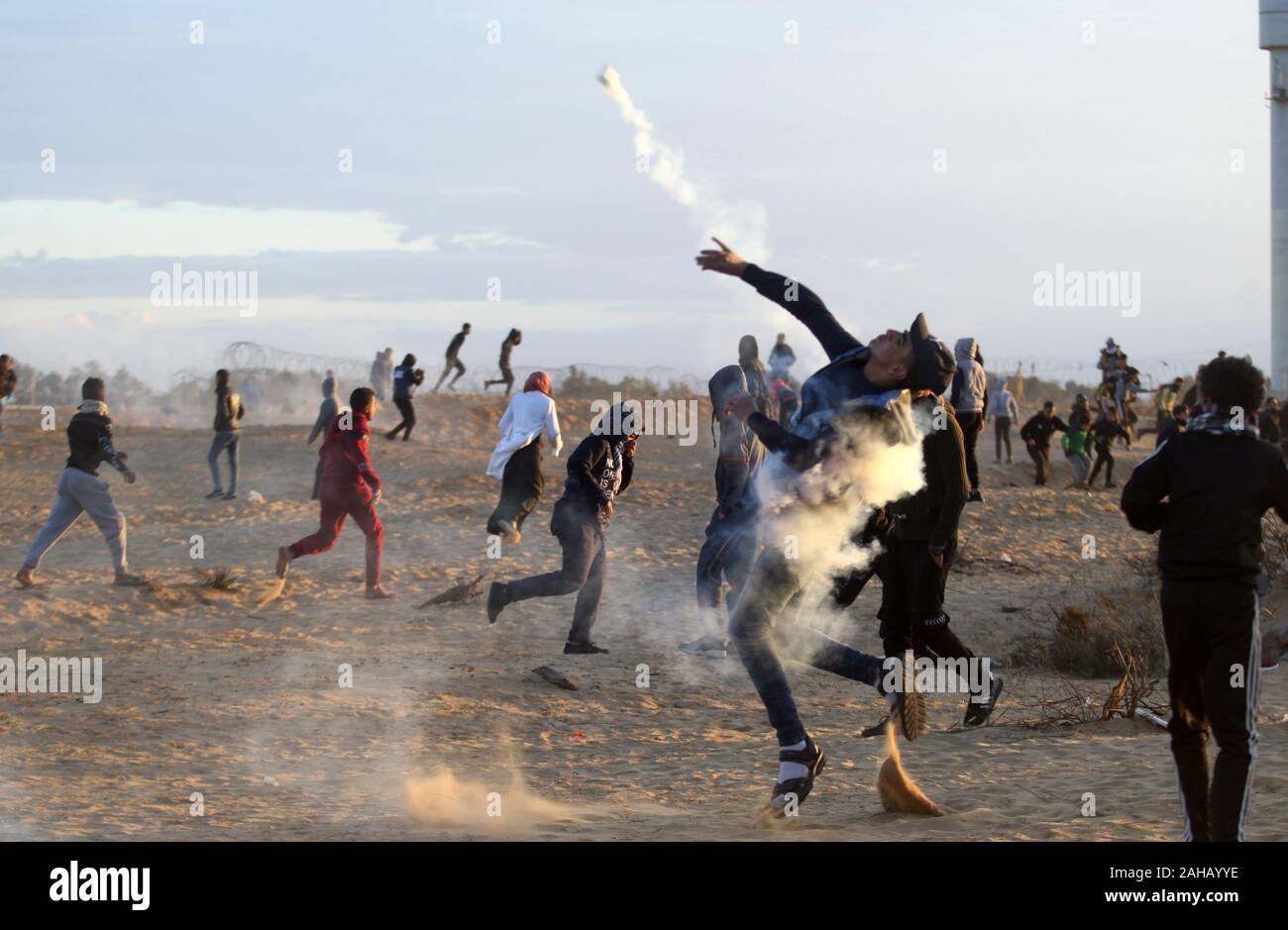 Rafah, Gaza. 27th Dec, 2019. A Palestinian protester throws back a tear gas canister fired by Israeli forces during clashes following a demonstration along the border with Israel east of Rafah in the southern Gaza strip on Friday, December 27, 2019. Palestinians in Gaza will scale back protests along the fortified border with Israel, factions in the strip said on Thursday. Photo by Ismael Mohamad/UPI Credit: UPI/Alamy Live News Stock Photo
