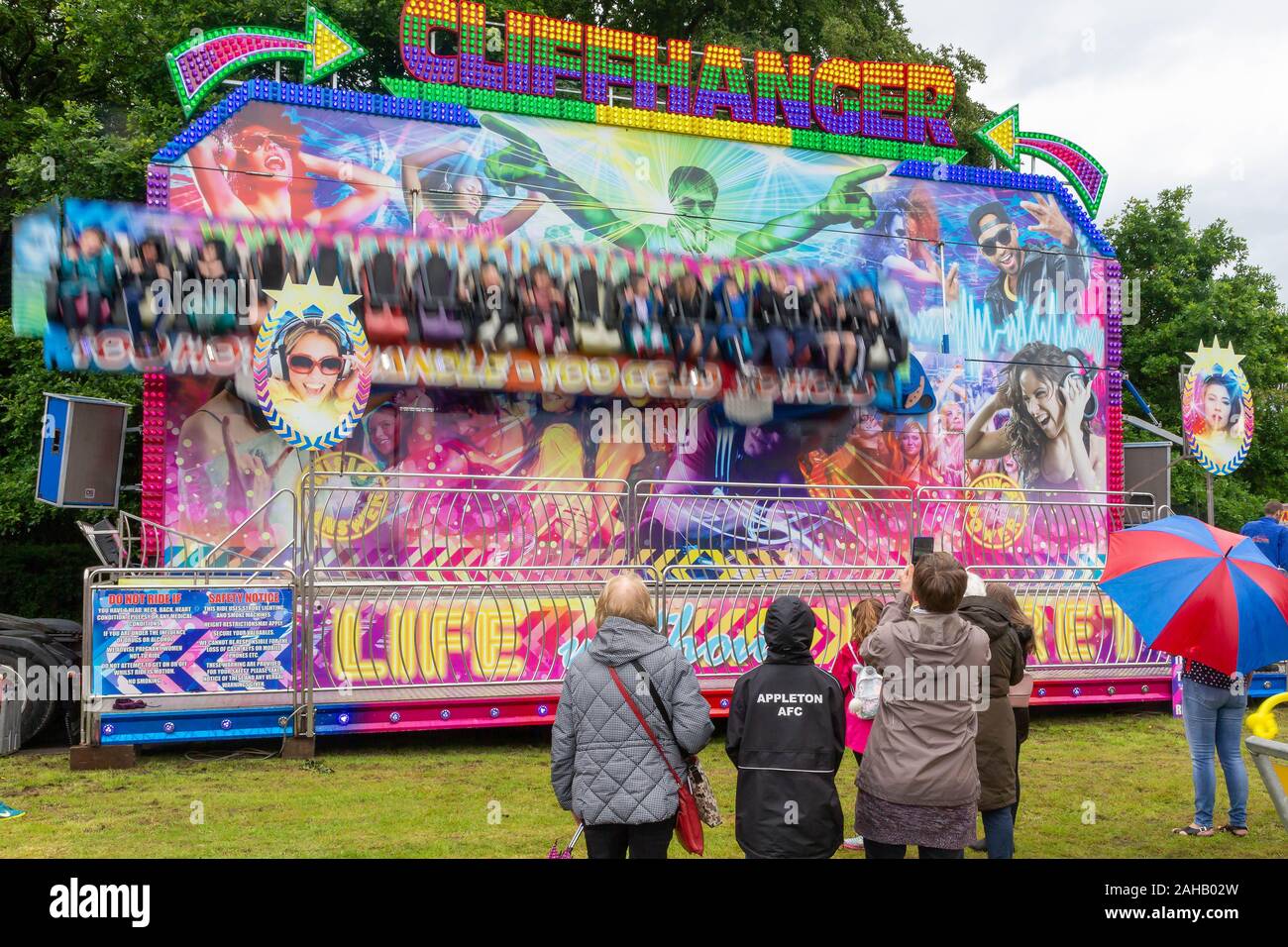 People watching the Cliffhanger fairground ride in wet weather in summer after the Thelwall Rose Queen procession 2019 Stock Photo