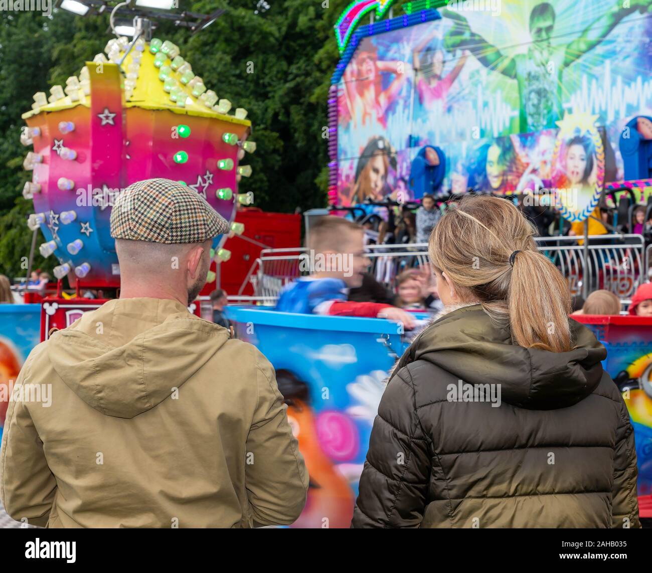 Mum and dad watching their child on a tea cup ride at a summer fair  after the Thelwall Rose Queen procession 2019 Stock Photo