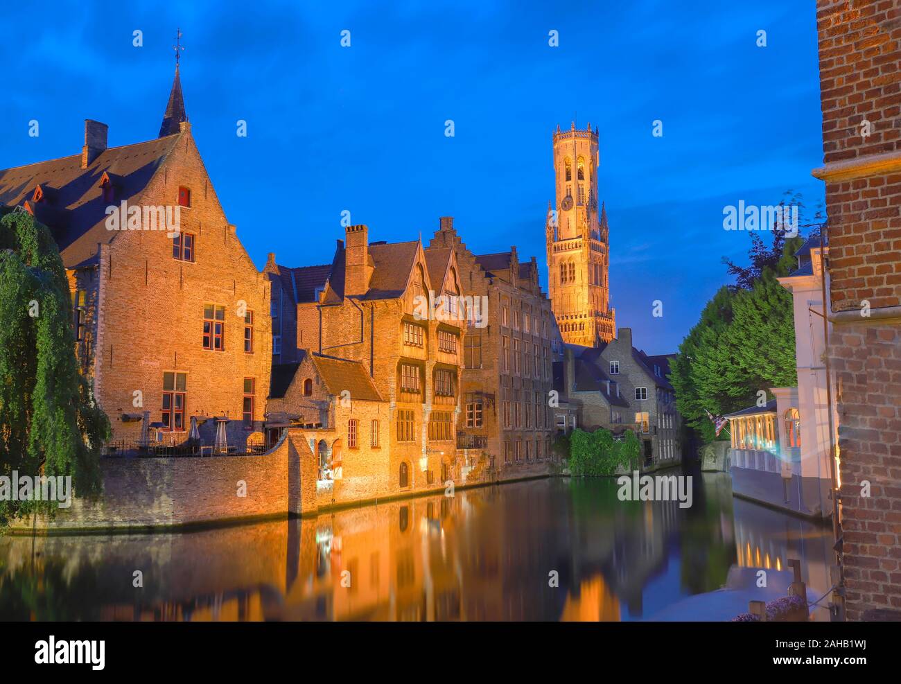 Famous view of Bruges tourist landmark attraction - Rozenhoedkaai canal with Belfry and old houses along canal with tree in the night. Belgium Stock Photo