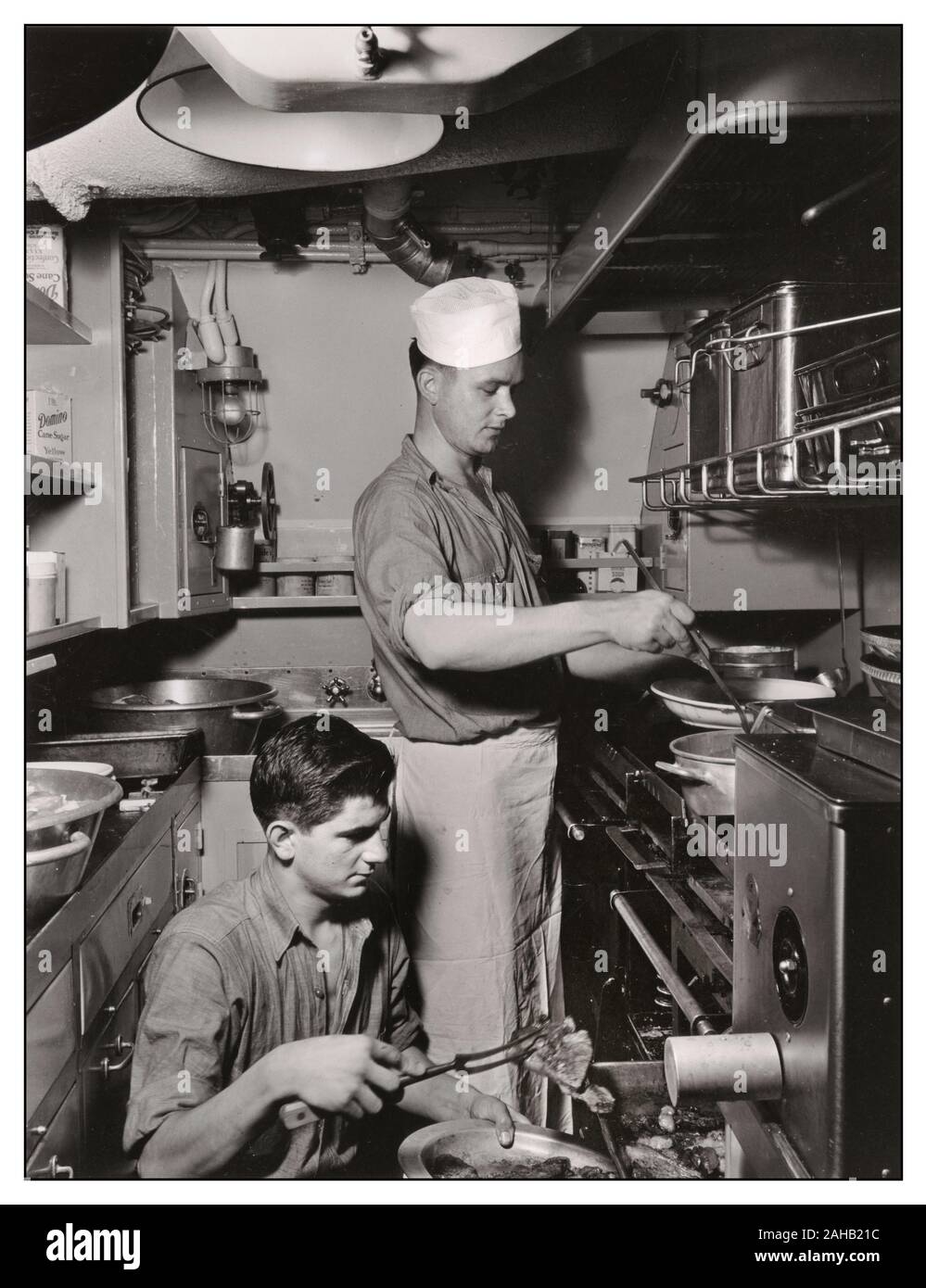 World War II USA American Submarine Life with cook aboard a submarine ladling out a meal with a new stainless steel utensil. August, 1943 Two soldiers preparing meal in submarine galley. military personnel Second World War WW2 American Navy Submarine Galley kitchen food preparation Stock Photo