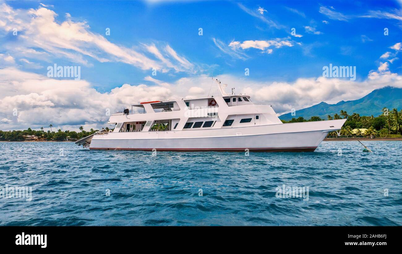 A beautiful private motor yacht, which is also used as a liveaboard dive vessel, is anchored in front of a tropical island in the Philippines. Stock Photo
