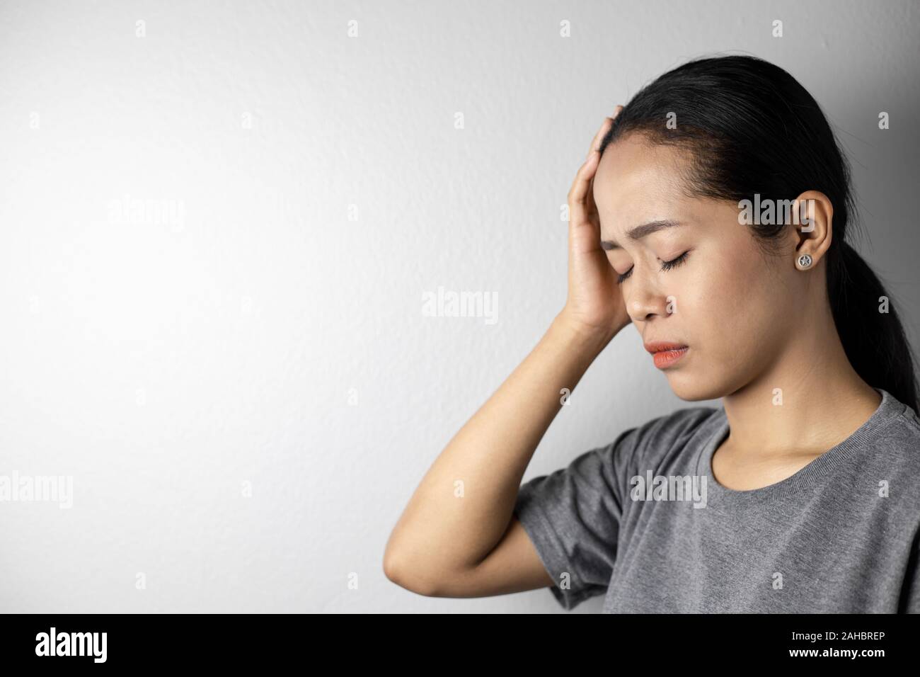 Young woman with of stress and headaches on a gray background. Asian woman with a headache. Women with a lot of stress. Stock Photo