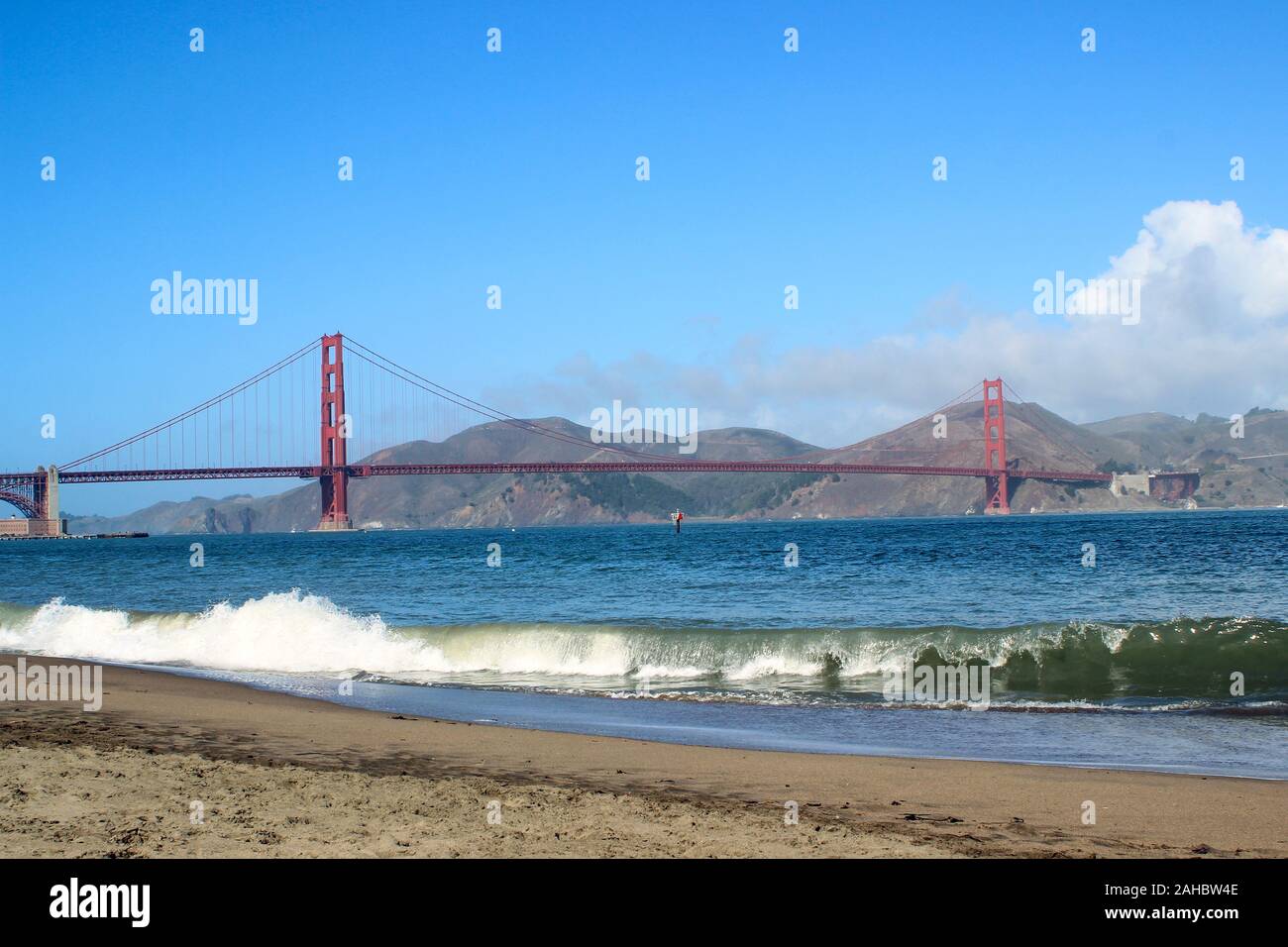 International orange Golden Gate Bridge with waves breaking on to Crissy Field recreational area beach in front. San Francisco, United States. Stock Photo