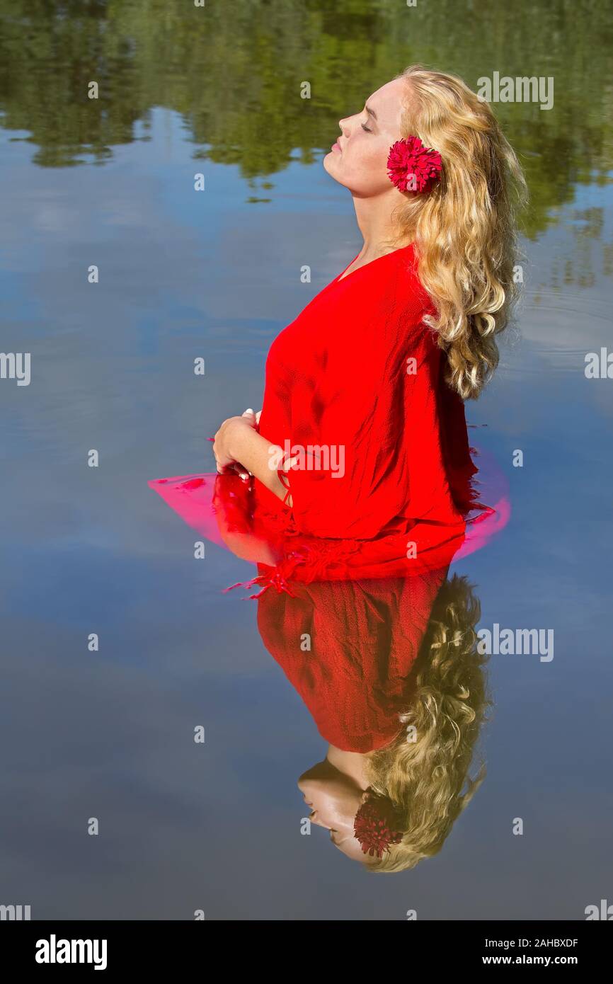 Attractive blonde dutch woman in red clothes standing in water with mirror image Stock Photo