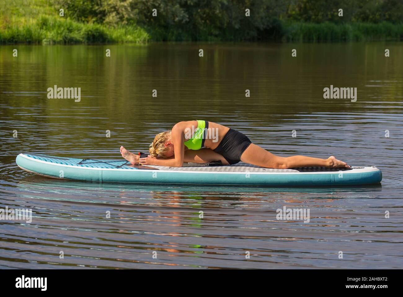Young caucasian woman lying in splits on paddle board in water Stock Photo