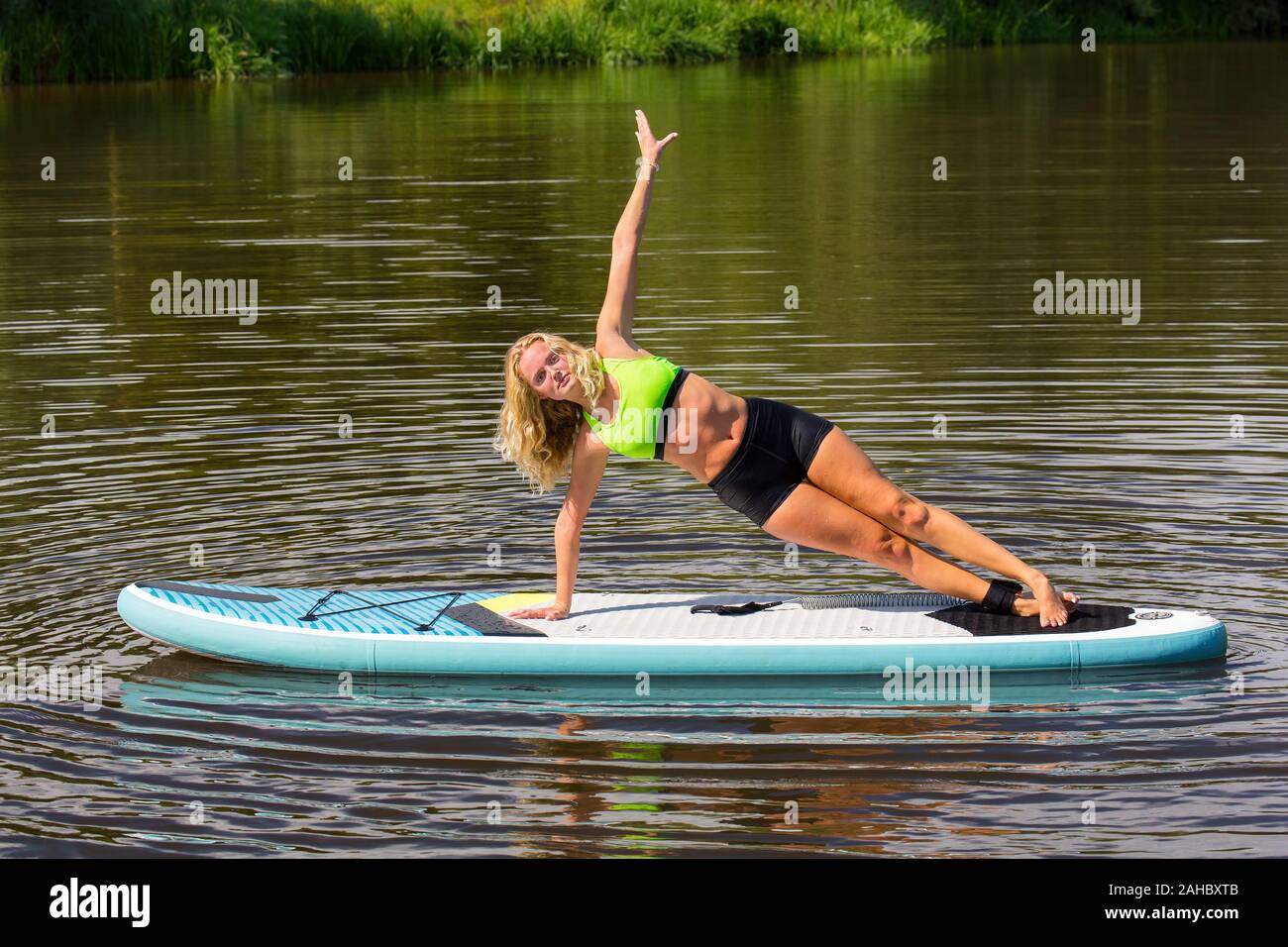 Young european woman planking sideways on SUP in lake Stock Photo