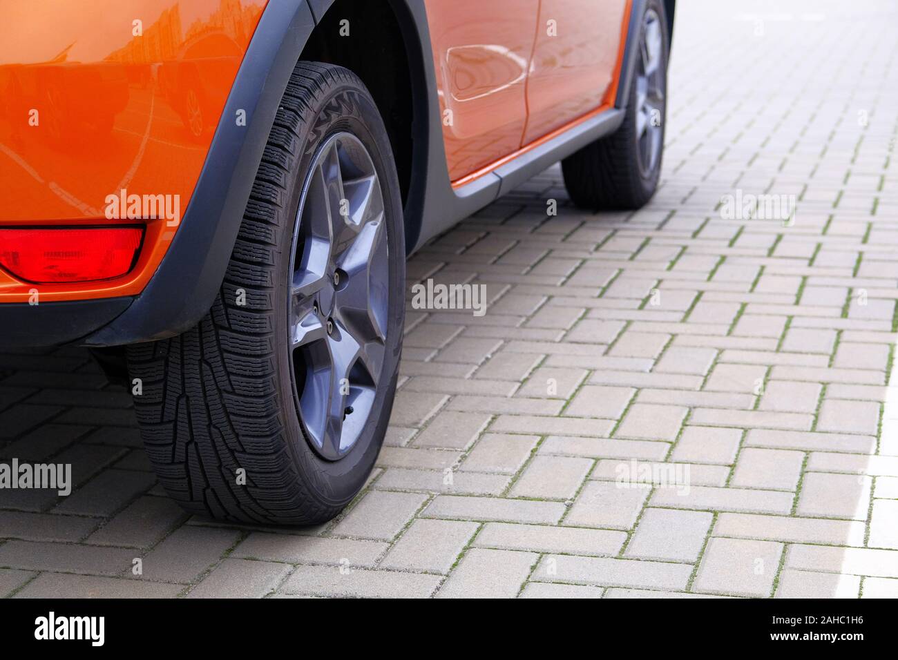 Orange car is parked in its parking spot in city. Close up car wheel, urban environment. Stock Photo