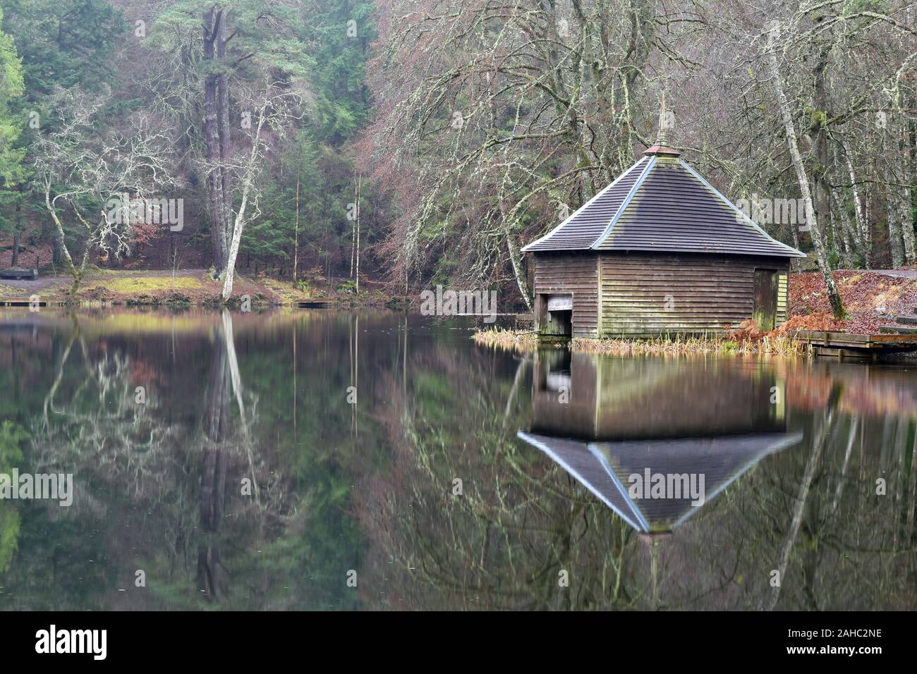 Loch Dunmore near Pitlochry in Perthshire, Scotland. Boathouse and trees reflected perfectly in calm waters of the loch. Taken in winter. Stock Photo