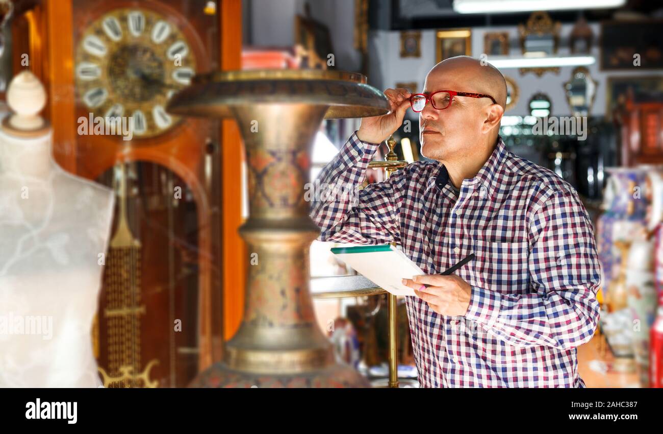 focused middle aged man owner of antiques shop inventorying vintage goods Stock Photo