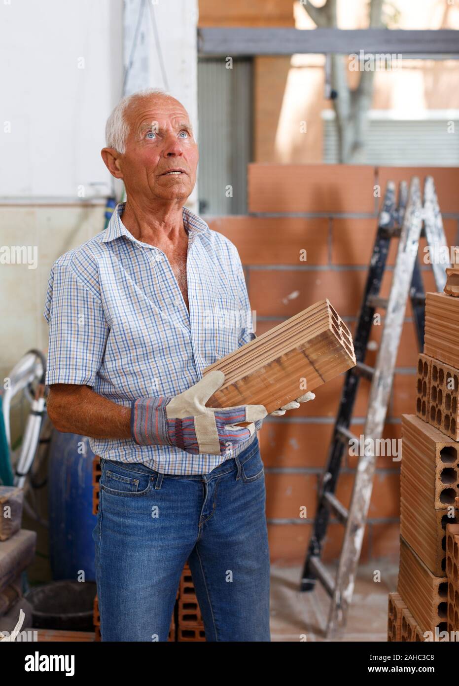 Skillful older man inspecting brick for installing wall in building under construction Stock Photo
