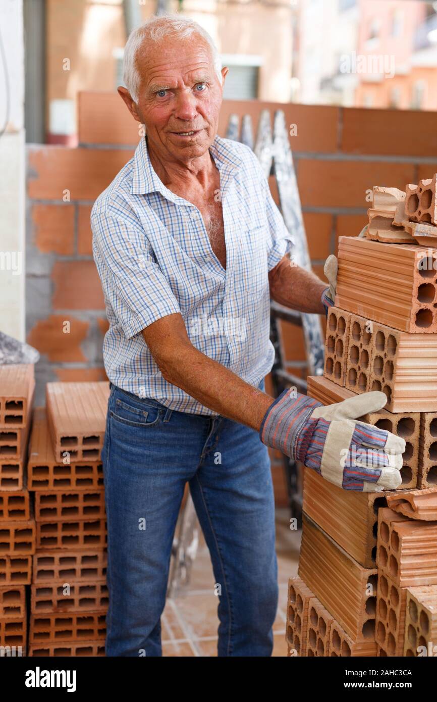 Skillful older man inspecting brick for installing wall in building under construction Stock Photo