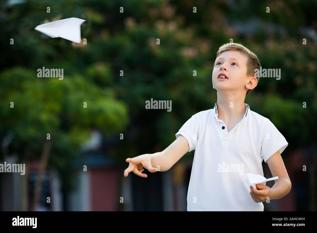 happy boy playing with simple paper airplane toy on sunny day in town ...