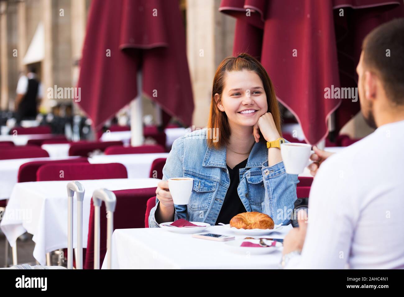 Positive man and woman sitting with coffee and talking at the table in ...