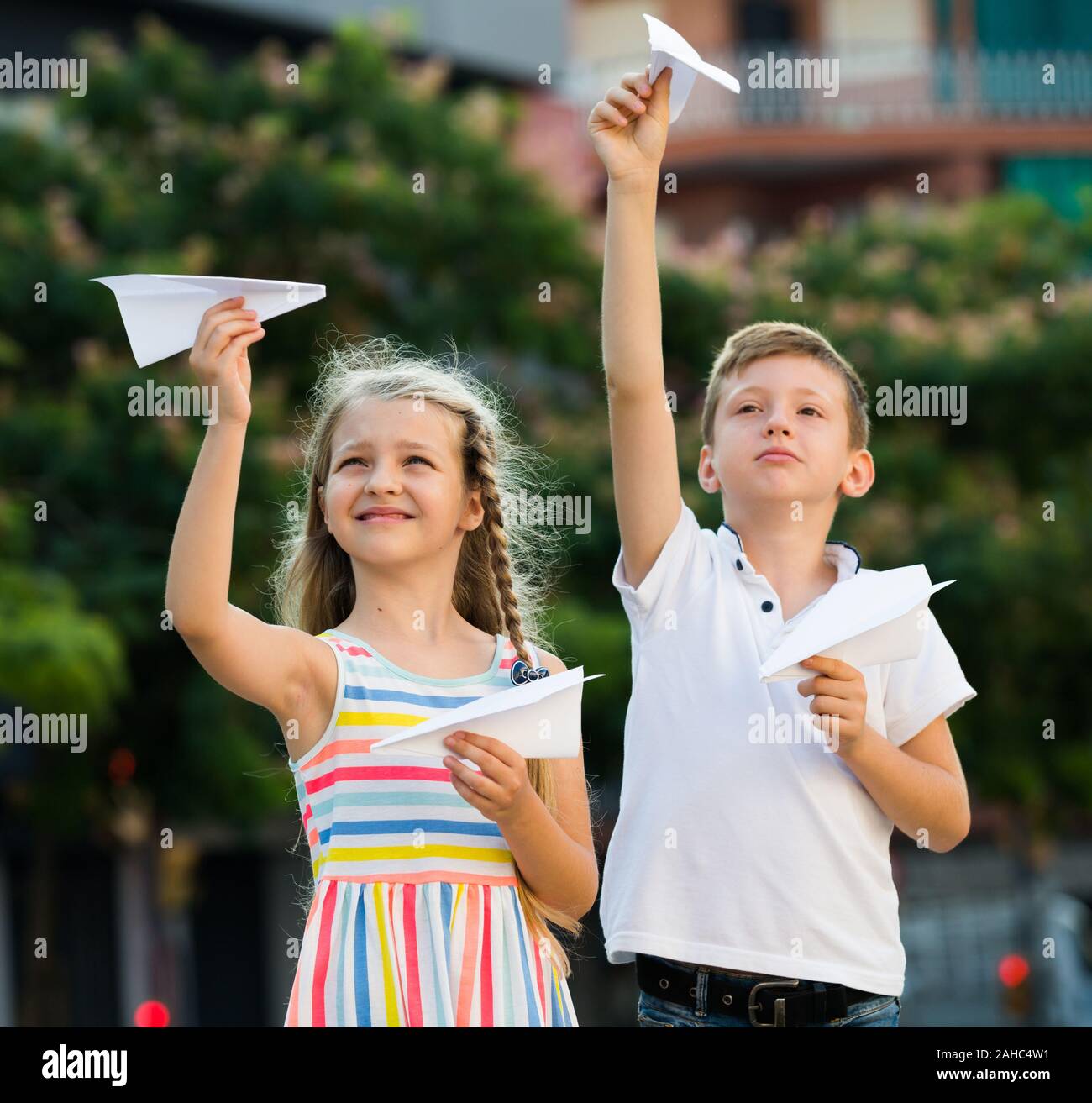 two happy kids playing with simple paper planes on sunny day in town ...