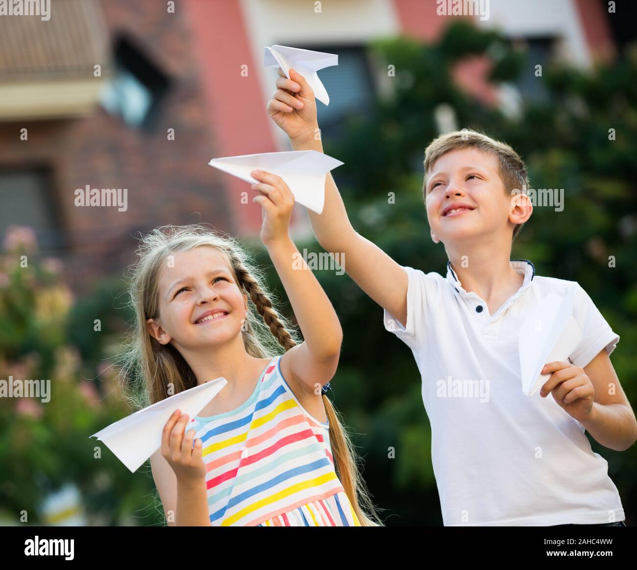 two happy kids playing with simple paper planes on sunny day in town ...