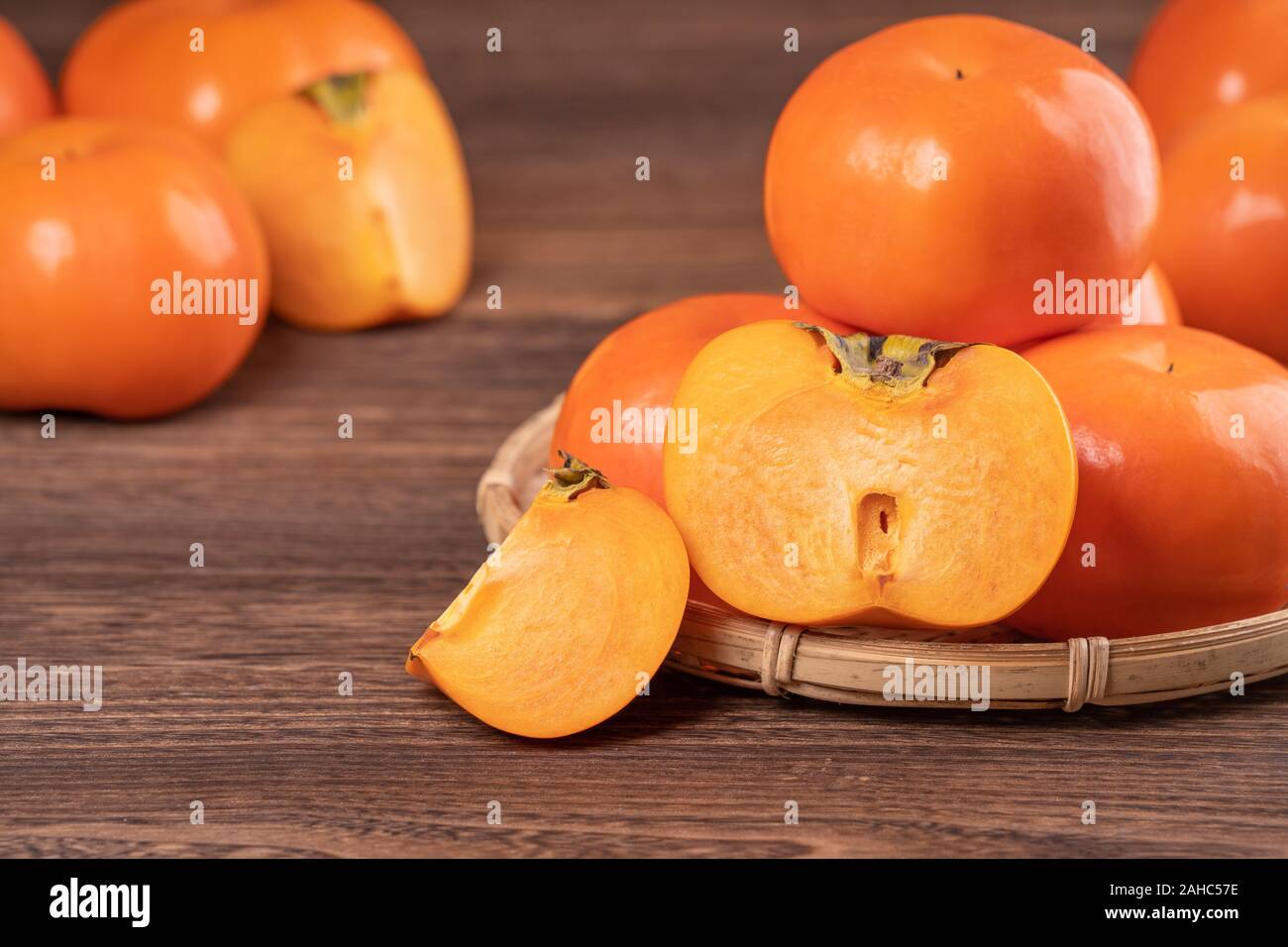 Fresh, beautiful orange color persimmon kaki on bamboo sieve over dark wooden table. Seasonal, traditional fruit of Chinese lunar new year, close up. Stock Photo