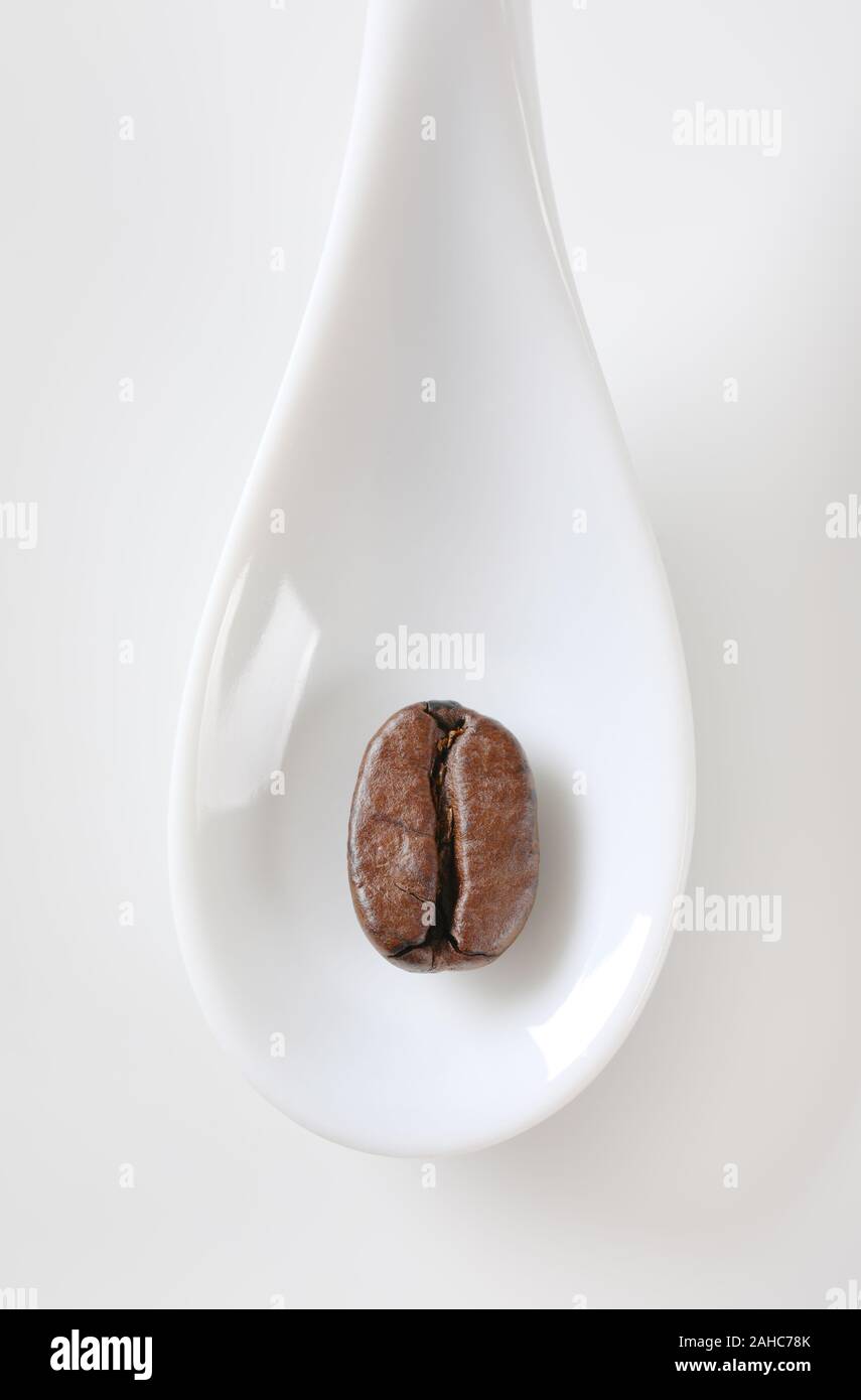Overhead view of a roasted coffee bean on white porcelain spoon Stock Photo
