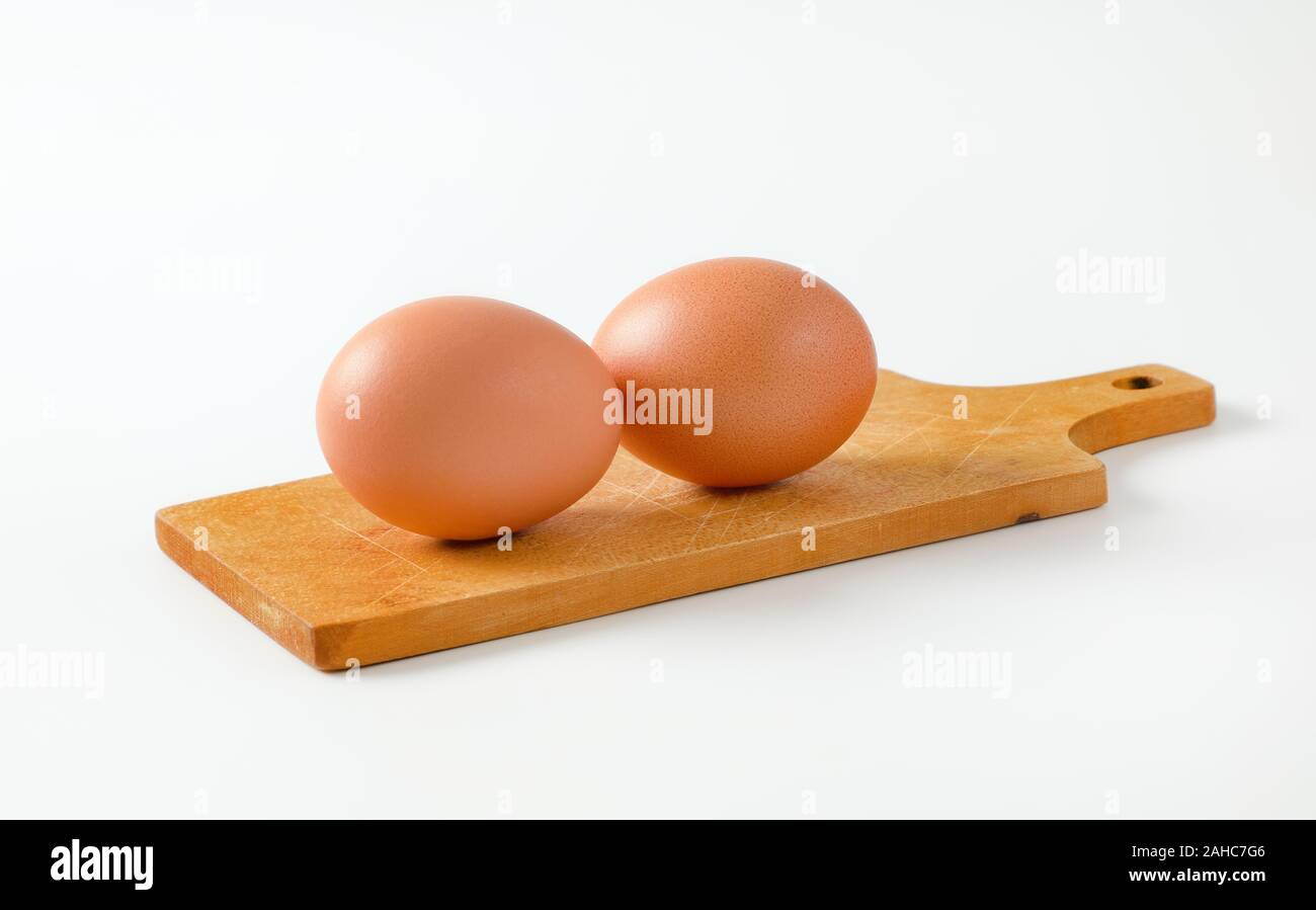Two brown eggs on wooden cutting board Stock Photo