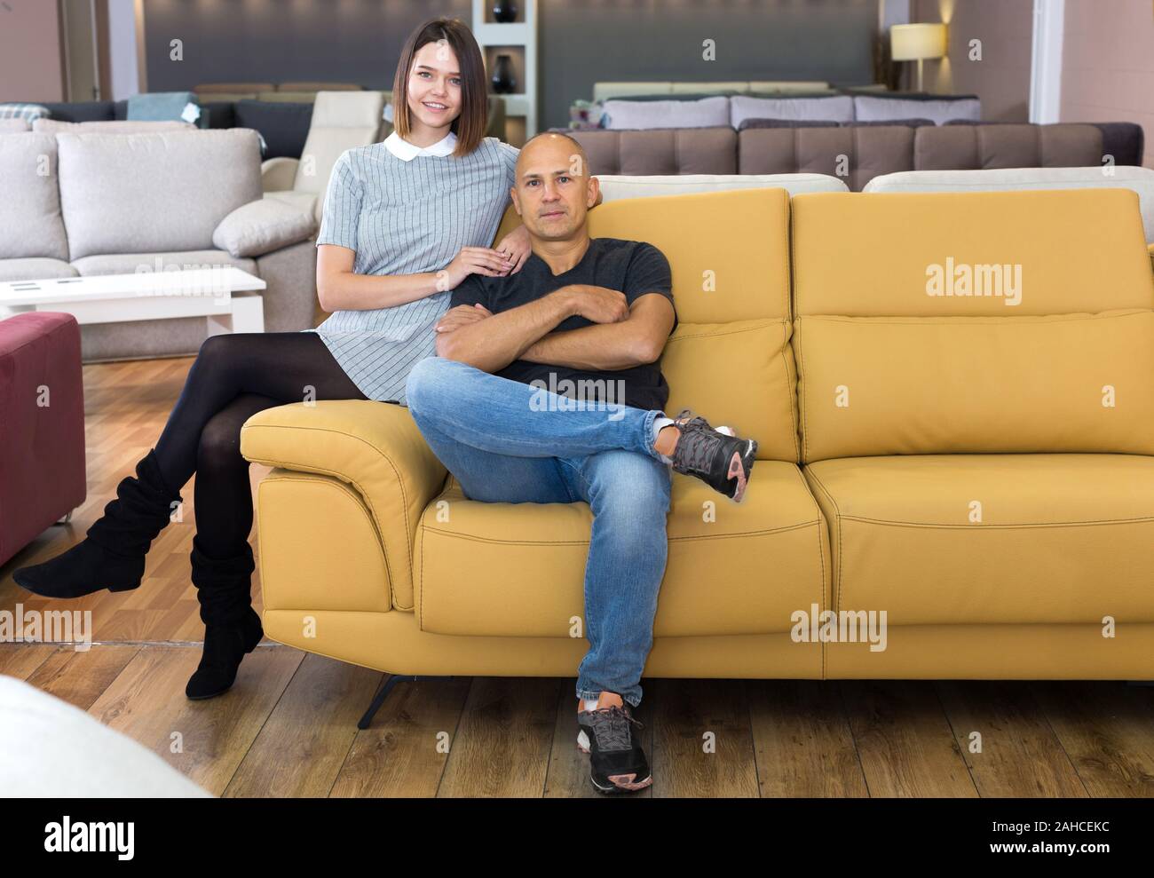 Happy Husband And Wife Sitting On Bright Yellow Couch In Furniture