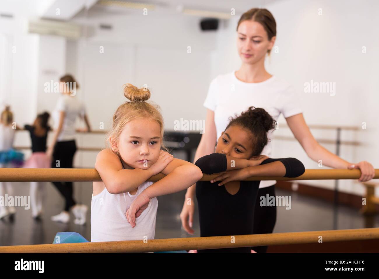 Portrait of two little girls and choreography teacher near ballet barre teacher in dance school