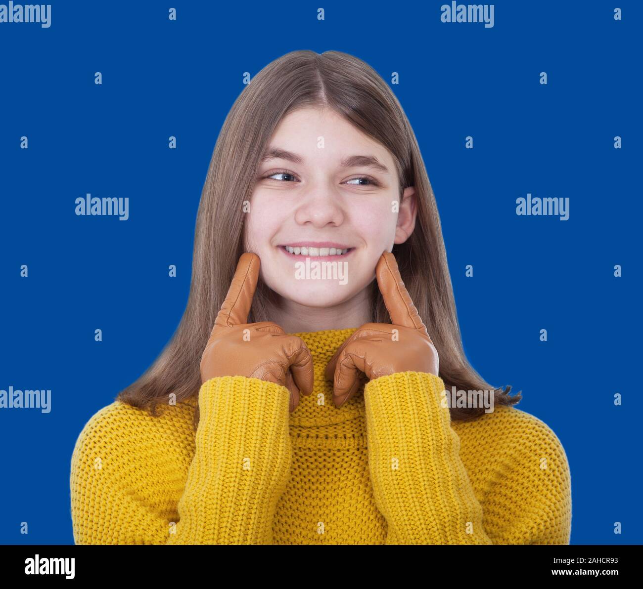 Smiling girl in a yellow sweater and yellow leather gloves on a blue background Stock Photo