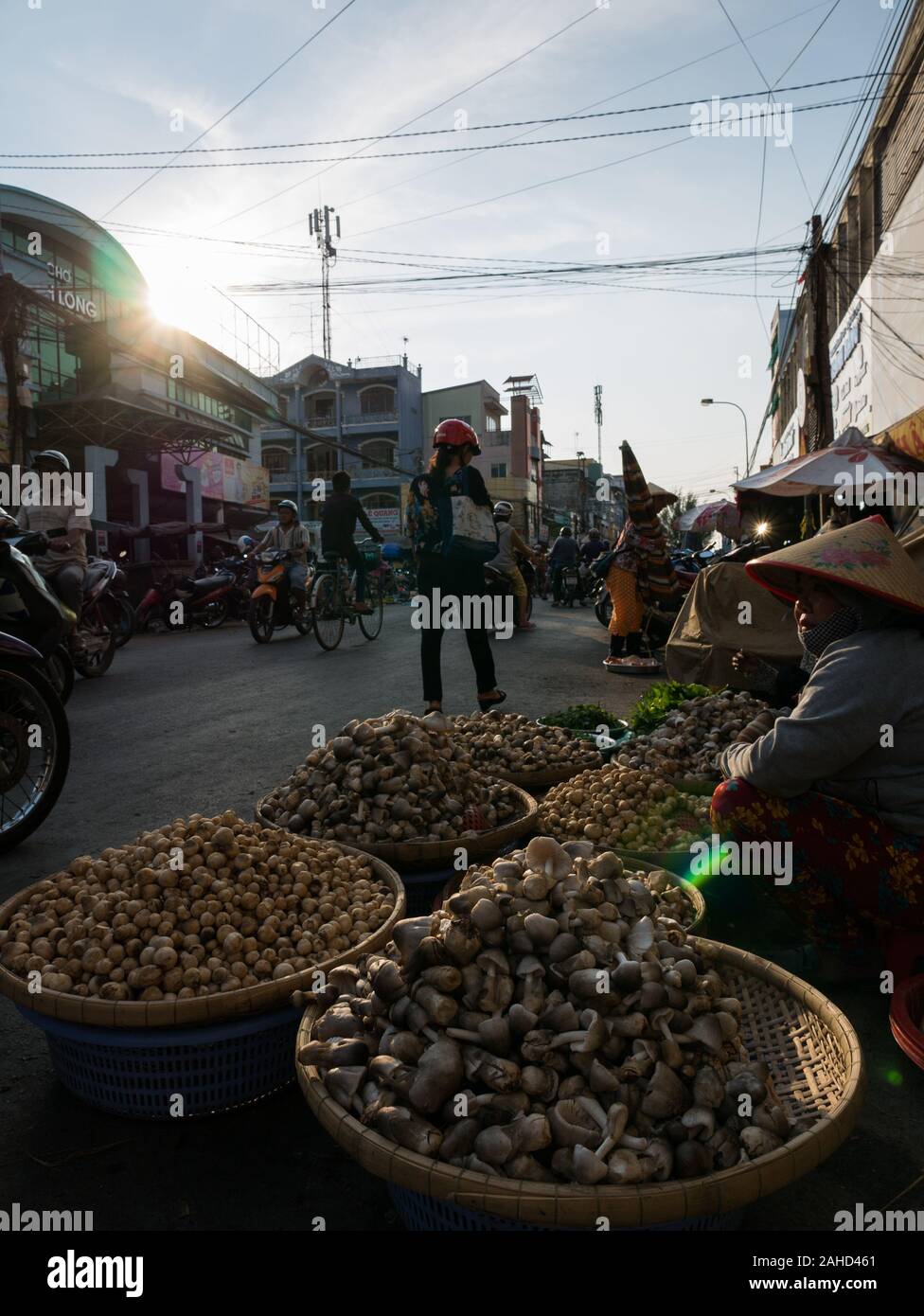 Vietnamese street vendor selling mushrooms at busy fruit market from low angle with backlight Stock Photo